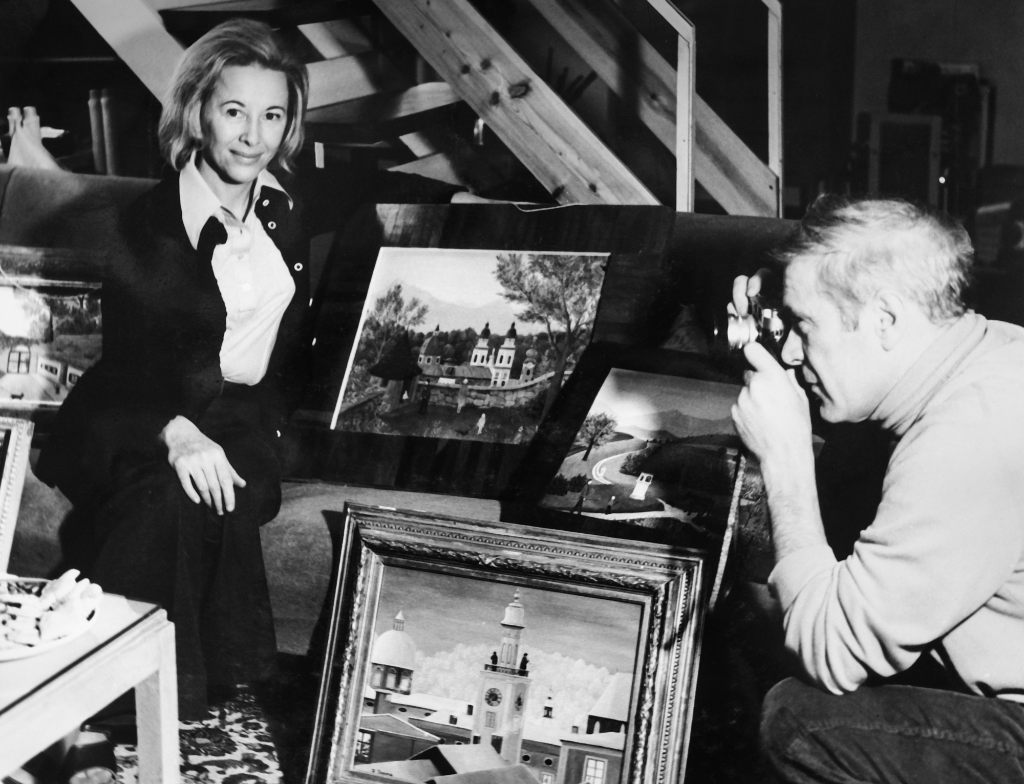 Josef fotografiert Regine vor ihren Gemälden